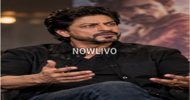 Bollywood-style actor in a dark shirt speaking thoughtfully during an interview in front of a film poster.