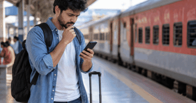 Traveller checking a smartphone beside luggage on an Indian railway platform with a passenger train in the background