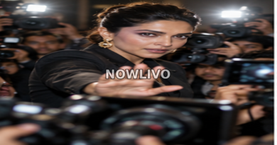 Glamorous celebrity figure raising a hand toward cameras and paparazzi at a crowded press event.